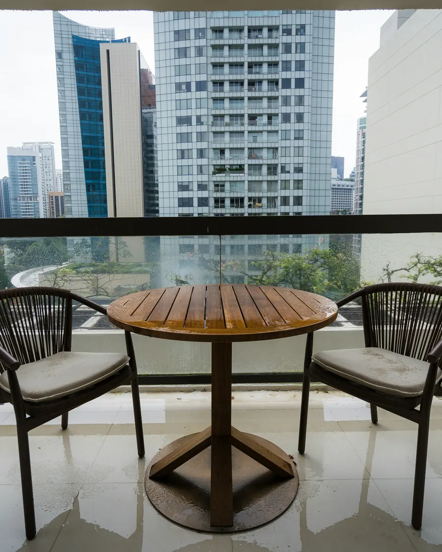A condo balcony with two chairs and a round teak table, looking out over city towers