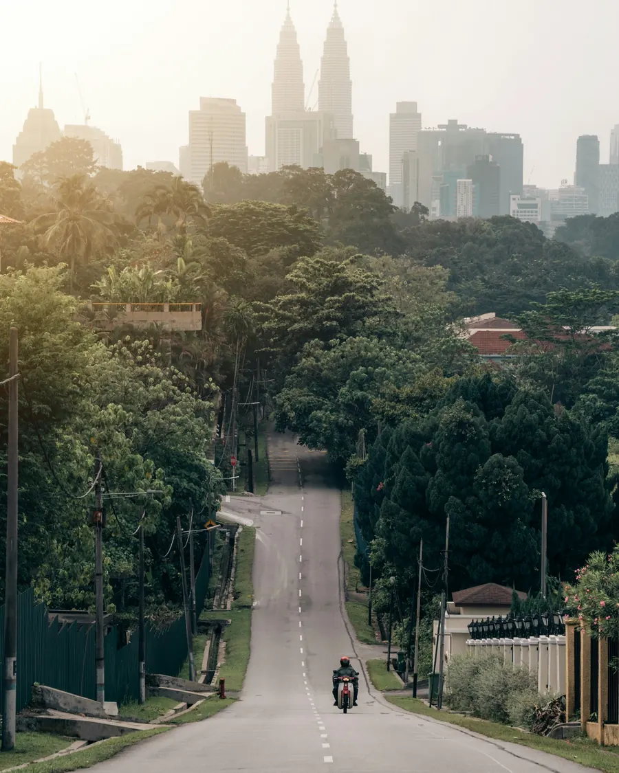A quiet tree-lined road in Bangsar, with the city towers rising through the haze
