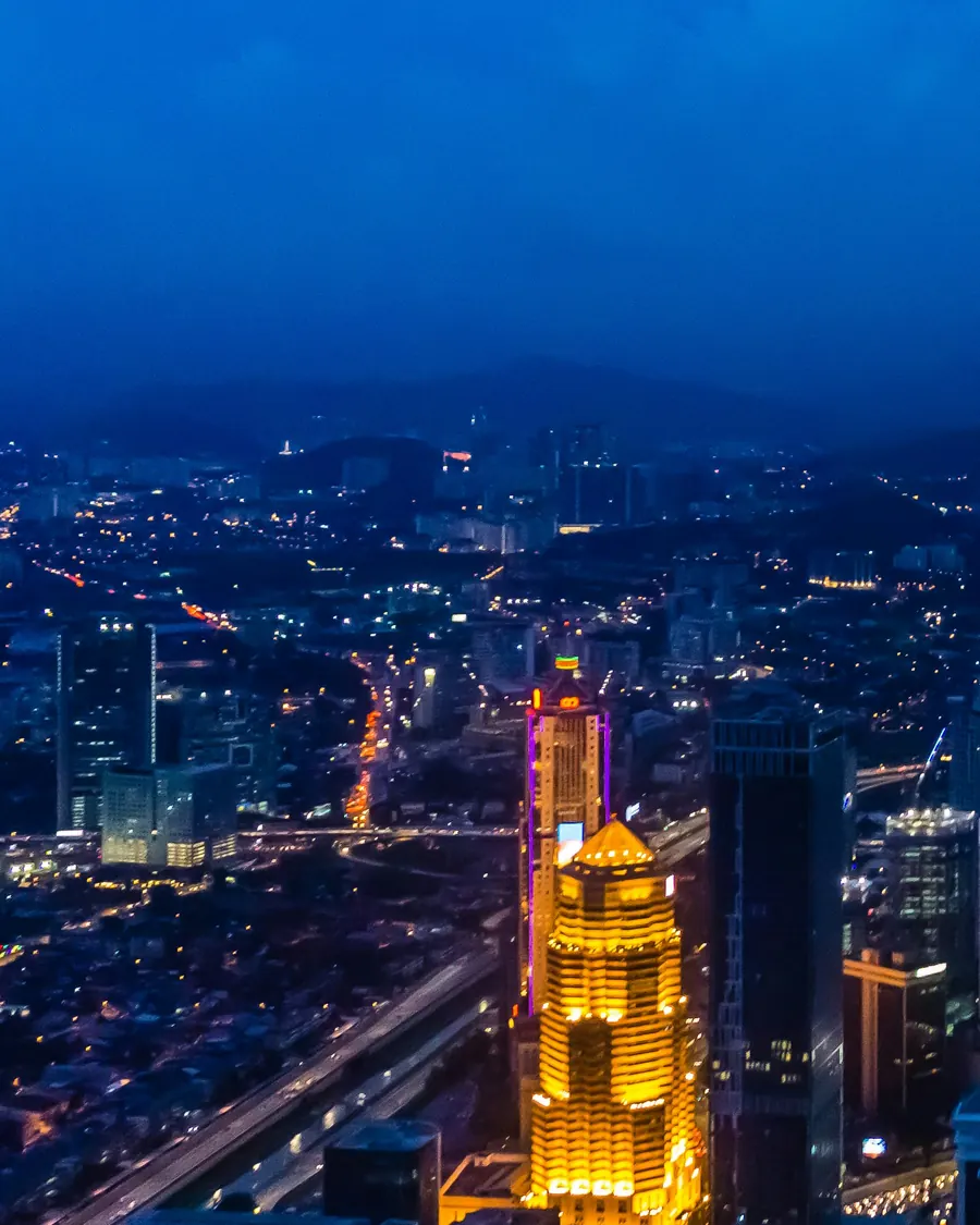 Central Kuala Lumpur at blue hour, with a golden-lit tower and streams of traffic