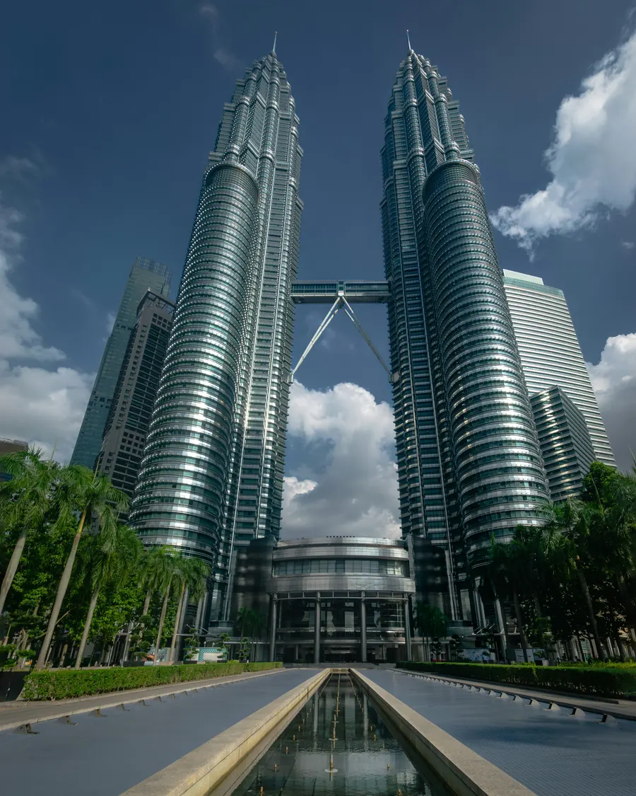 The Petronas Towers seen from the end of a long reflecting pool lined with palms